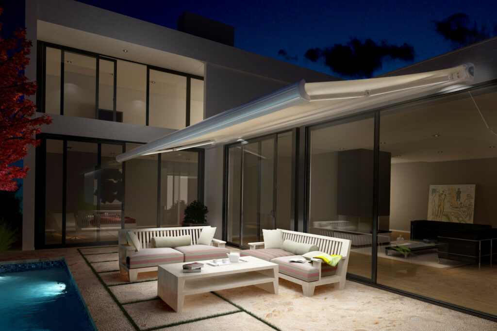 Store banne motorisé éclairé en soirée sur une terrasse contemporaine avec mobilier extérieur