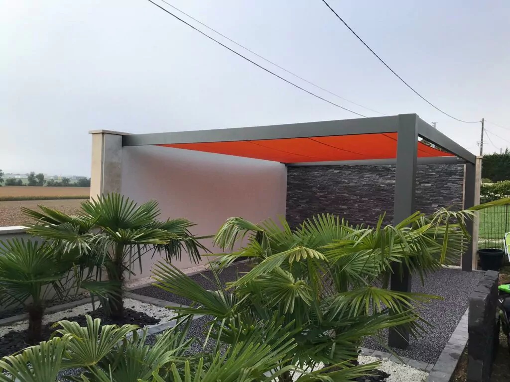 Carport contemporain à toile tendue orange, intégré dans un jardin paysager avec palmiers