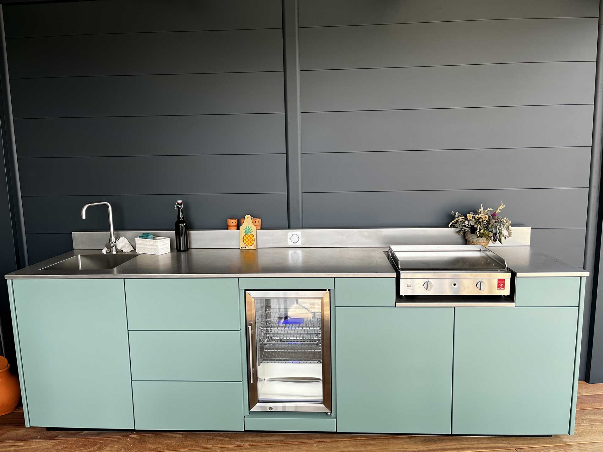 Cuisine extérieure sur-mesure en aluminium vert, avec évier, frigo, plancha et plan de travail en inox brossé sous pergola bioclimatique Cuisine extérieure sur-mesure en aluminium vert, avec évier, frigo, plancha et plan de travail en inox brossé sous pergola bioclimatique