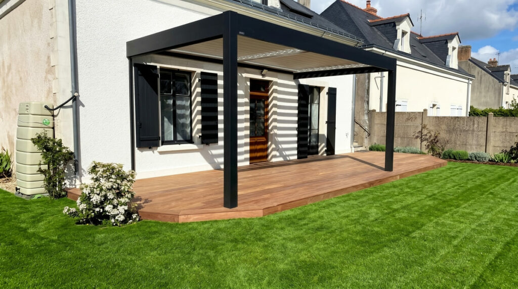 Terrasse en bois exotique sous une pergola bioclimatique anthracite, adossée à une maison de ville avec pelouse